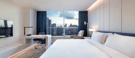 A modern hotel room with a large bed, a desk, a chair, and a TV.