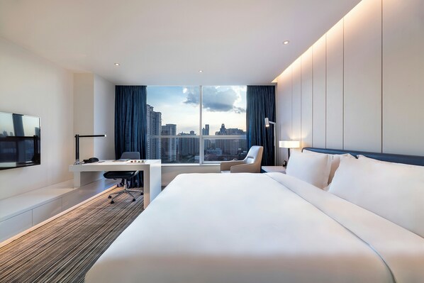 Una habitación de hotel moderna con una cama grande, un escritorio, una silla y un televisor.