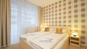 A hotel room with a large bed, two bedside tables, a nightstand, and a window with sheer curtains. - RentPlanet - Bliżej Morza (Kolobrzeg)