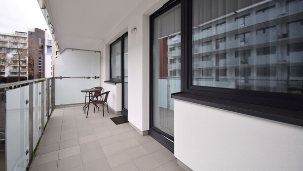 A balcony with a table and chairs, large windows, and a view of other buildings. - RentPlanet - Bliżej Morza (Kolobrzeg)