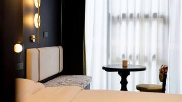 Een hotelkamer met een bed, nachtkastje met een kopje, een stoel en een wandlamp.