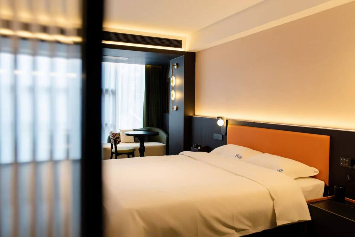 A hotel room with a bed, a nightstand, a lamp, a chair, and a small table.