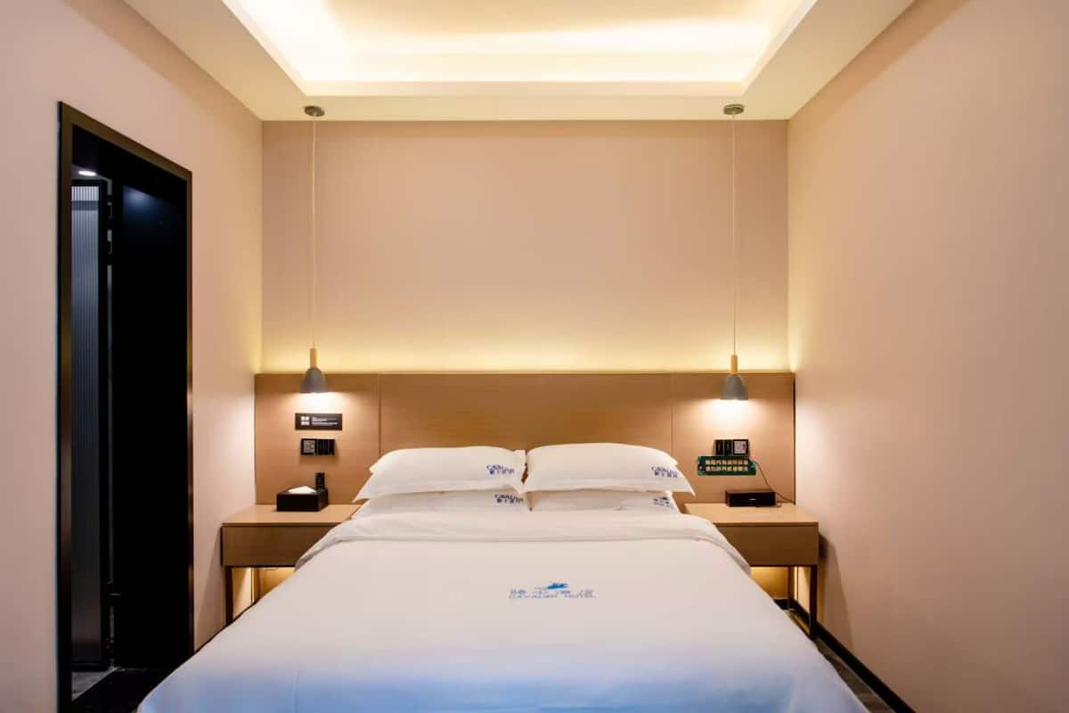A hotel room with a neatly made bed, two bedside tables with lamps, and a ceiling light.