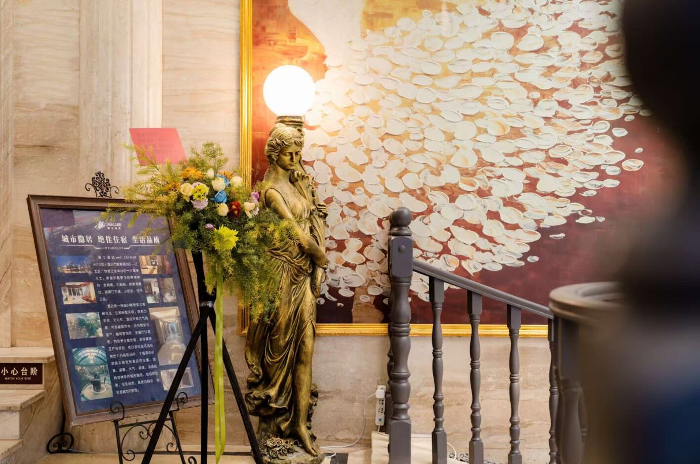 A statue with a floral arrangement in front, a wall with a textured pattern, and a sign with text.
