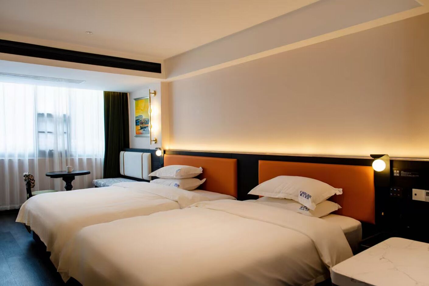 A hotel room with two beds, a small table, and a nightstand.