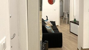 A modern living room with a black sofa, a dining area with a table and chairs, and a kitchen in the background. - Hermes Apartment with private parking (Trieste)