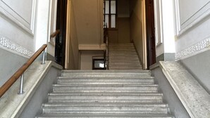 A grand staircase with a wooden handrail, leading to a room with a large window and a door. - Hermes Apartment with private parking (Trieste)