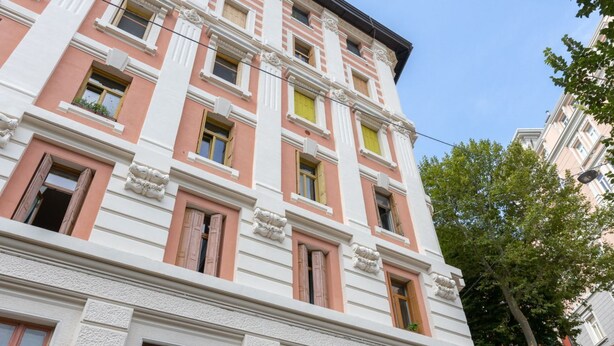 A multi-story building with a pink and white facade, multiple windows, and a brick base. - Hermes Apartment with private parking (Trieste)