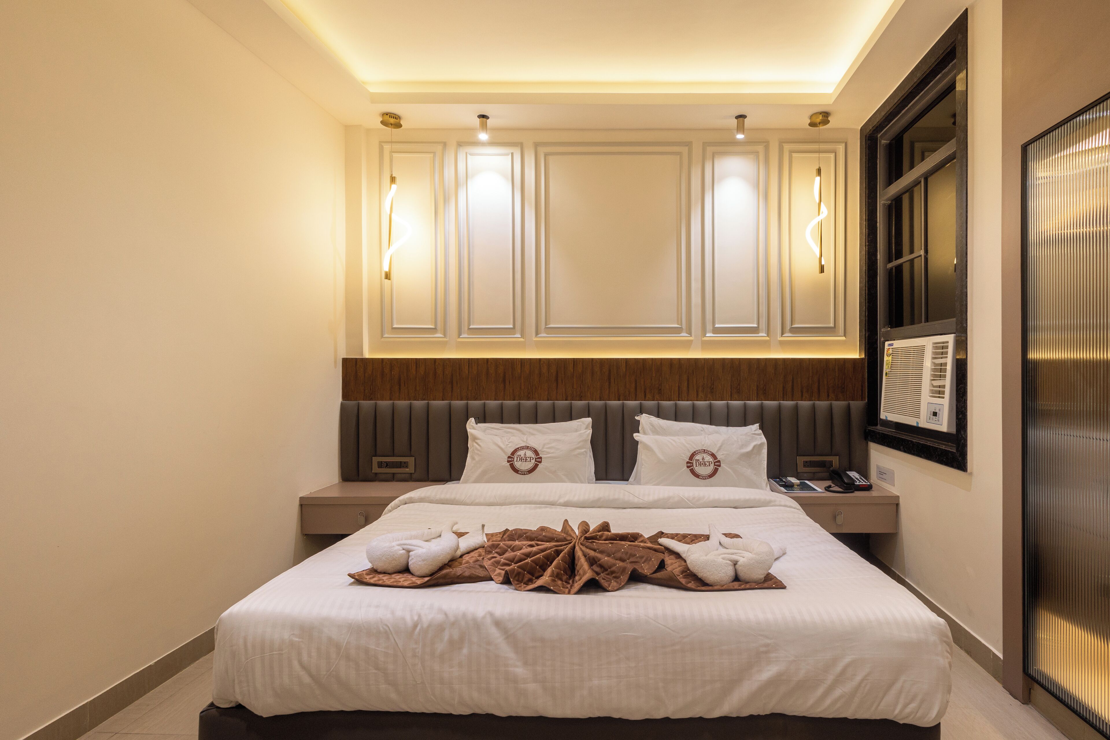 A hotel room with a large bed, a nightstand, a wall-mounted TV, and a window with blinds.