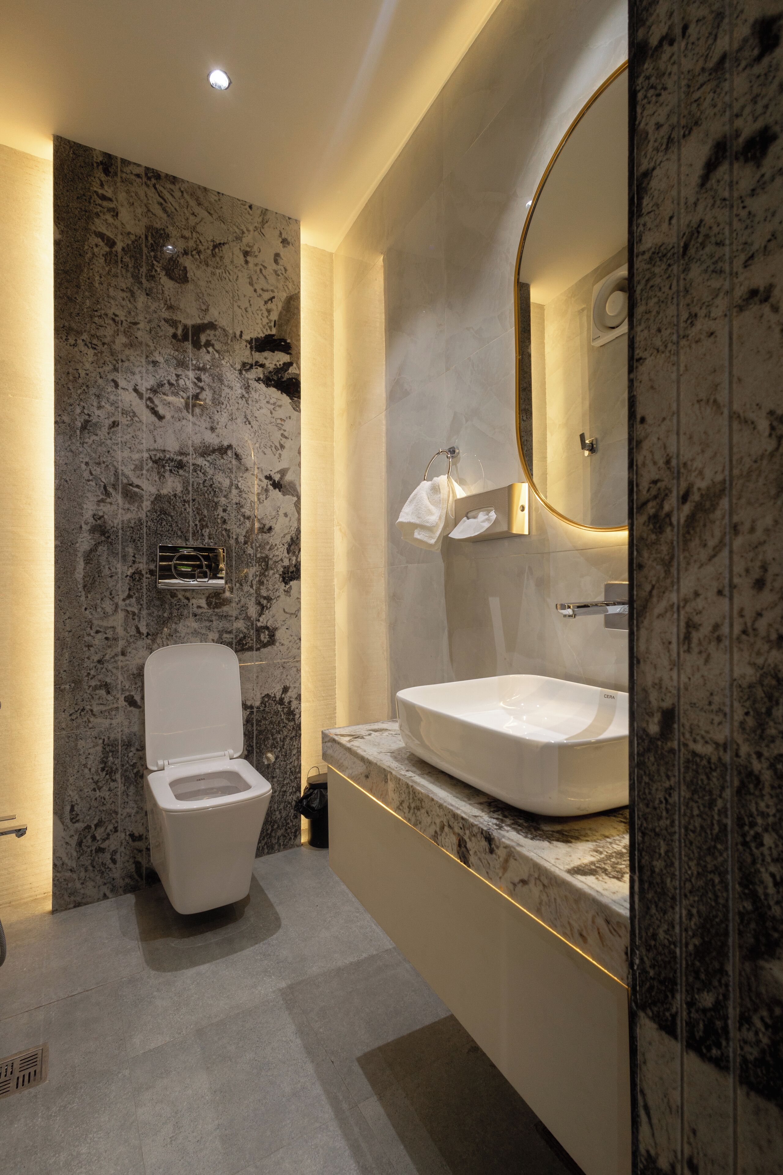 A modern bathroom with a marble wall, a white toilet, a large mirror, and a sink with a marble countertop.