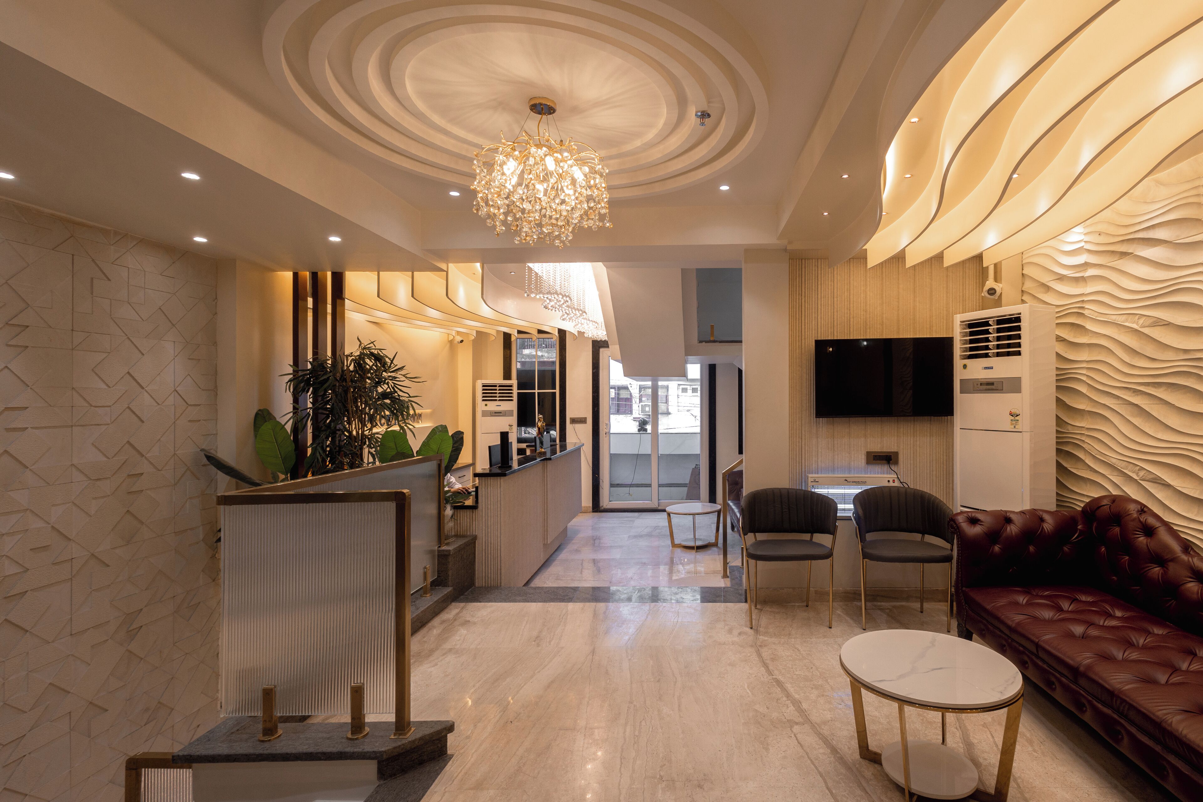 A modern hotel lobby with a reception desk, seating area, and a large TV screen.