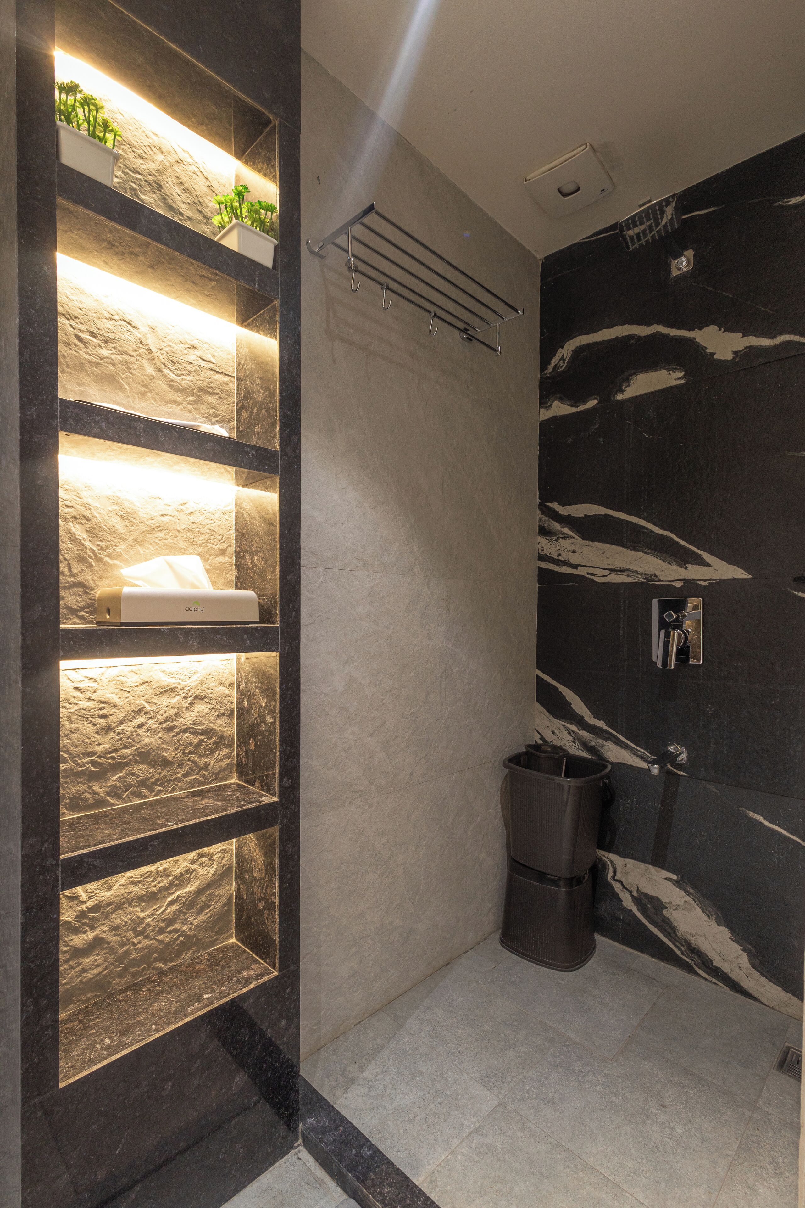 A modern bathroom with a stone shelf unit, a towel dispenser, and a black marble wall.