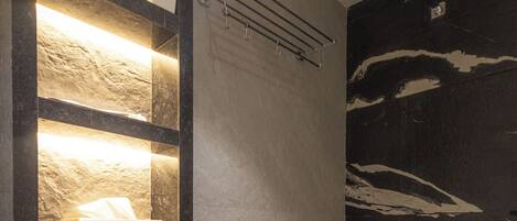 A modern bathroom with a stone shelf unit, a towel dispenser, and a black marble wall.