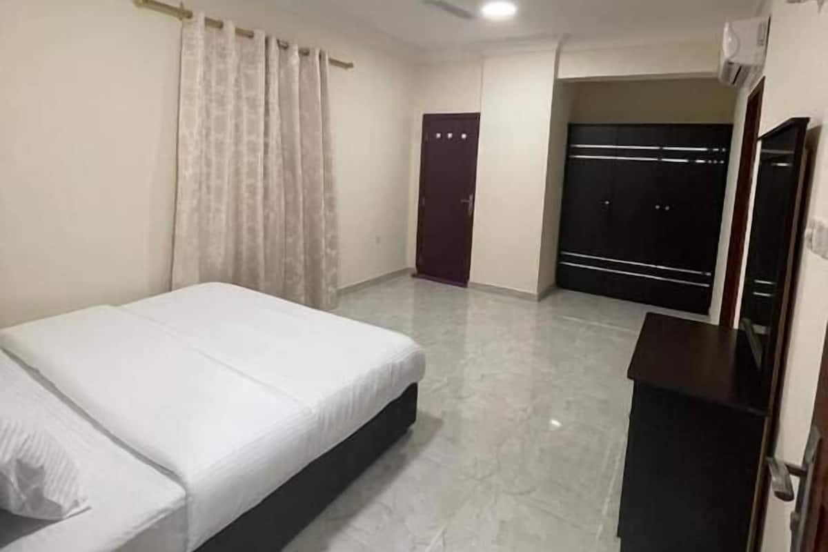 A hotel room with a bed, a desk, a wardrobe, and a ceiling fan.