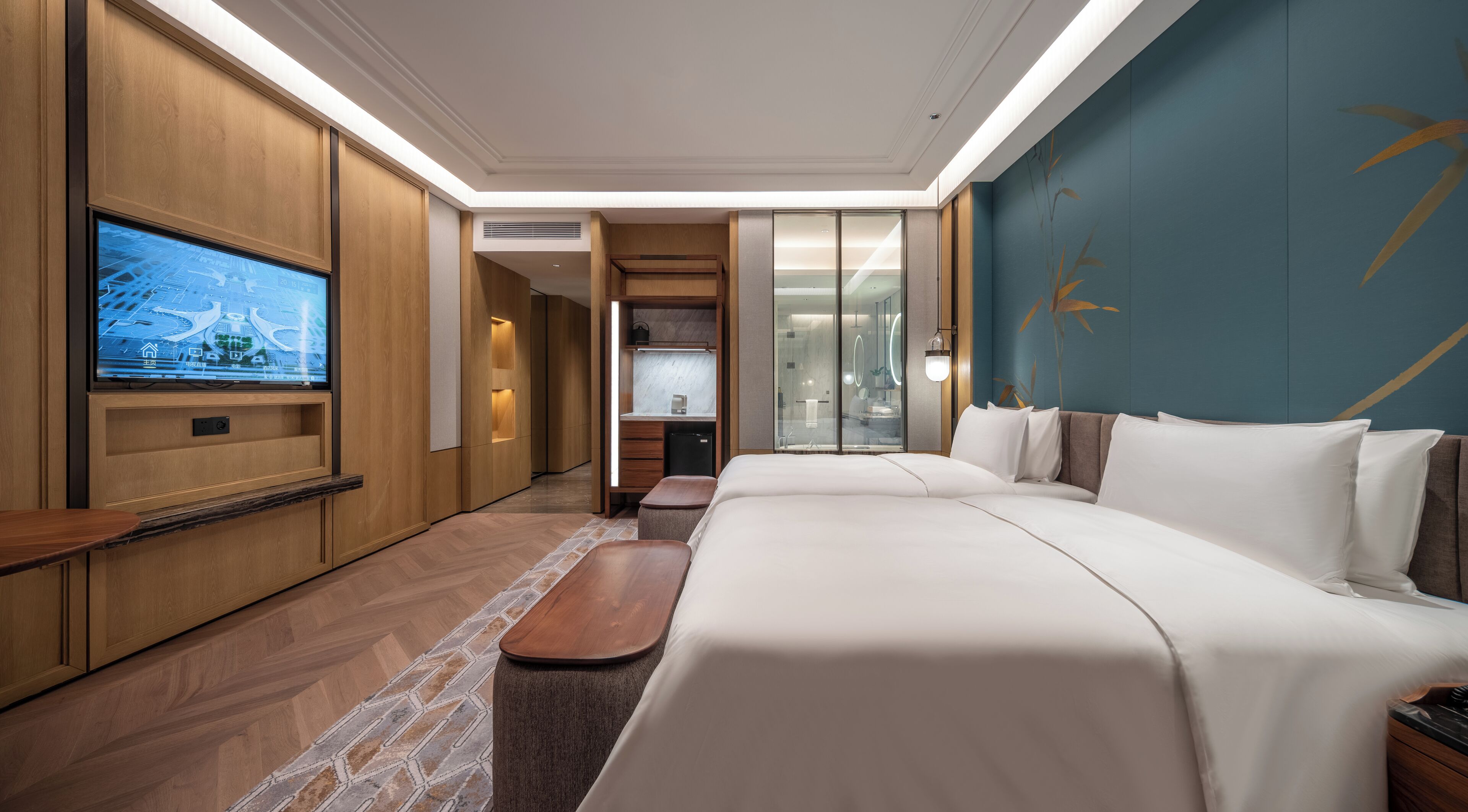 A modern hotel room with a large bed, a TV mounted on the wall, a desk, and a bathroom visible through a glass door.