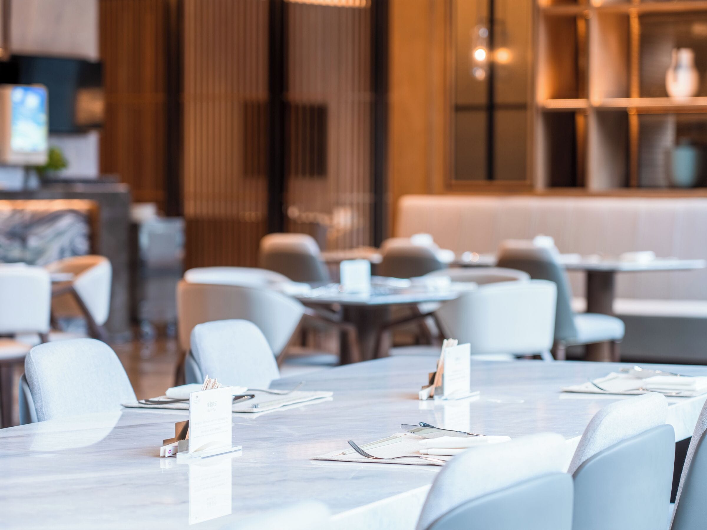 A modern restaurant with white tables and chairs, a wooden partition, and a bar area in the background.