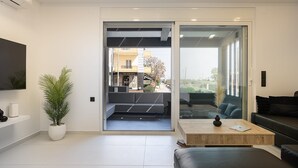 Una sala de estar moderna con un ventanal corredero que da a un área exterior, un televisor de pantalla plana en la pared, una planta en maceta y un sofá de cuero.