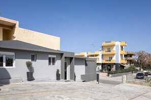 A modern building with a grey facade, a small entrance, and a stone-paved courtyard.