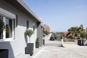 A modern building with large windows, a paved walkway, and a view of the sea. - Maxi Suite 75 with Jacuzzi (Gazi)