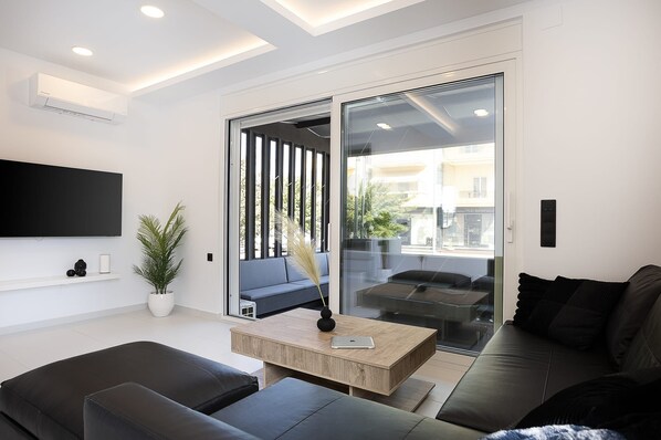 A modern living room with a flat-screen TV, a sofa, a coffee table, and a sliding glass door leading to a balcony.