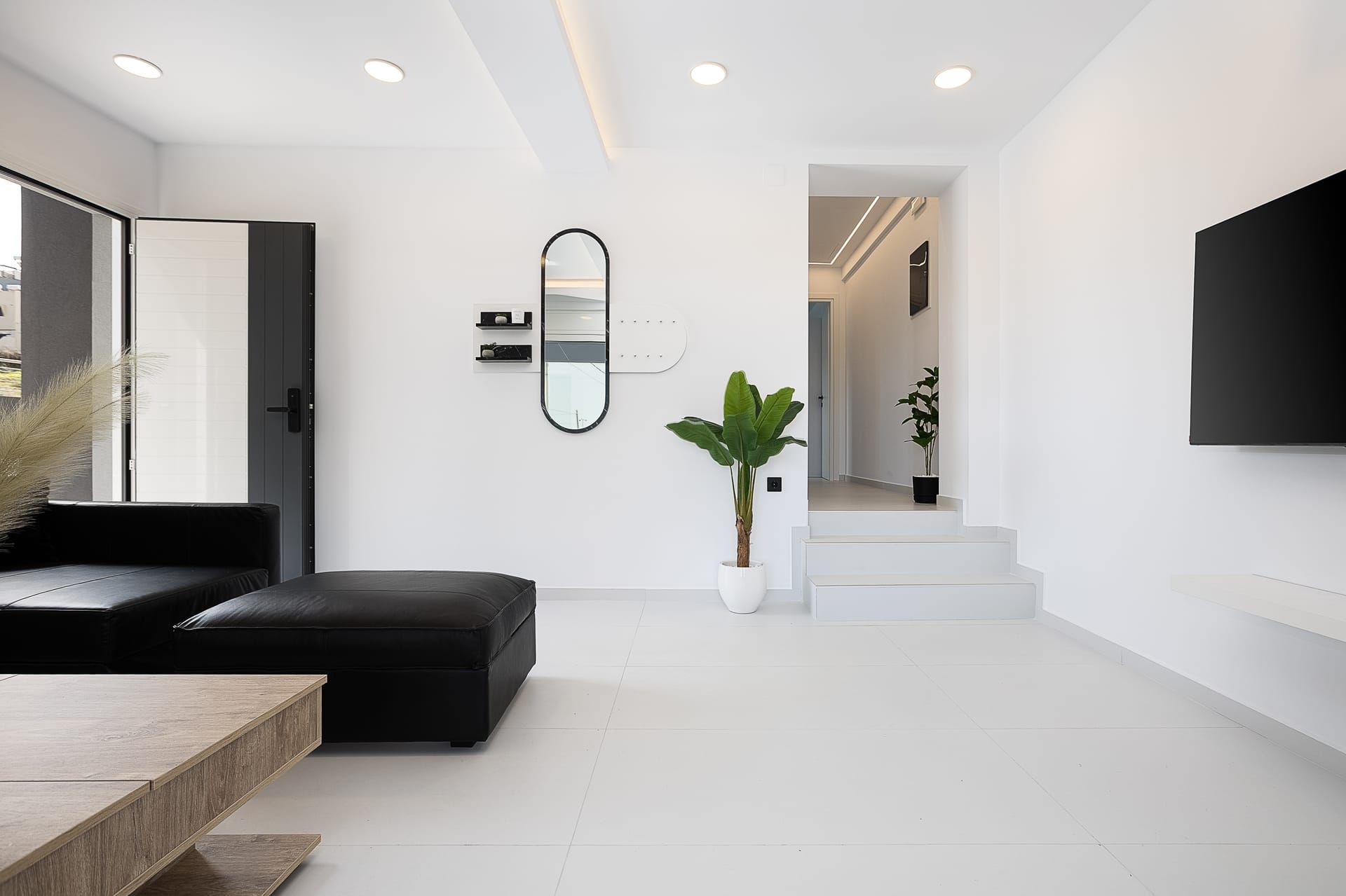 Una sala de estar moderna con un sofá negro, una mesa de centro de madera, una planta en maceta y un espejo grande en la pared.