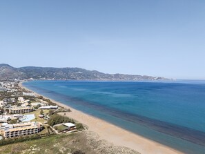A coastal view with a beach, buildings, and a hilly landscape in the background.