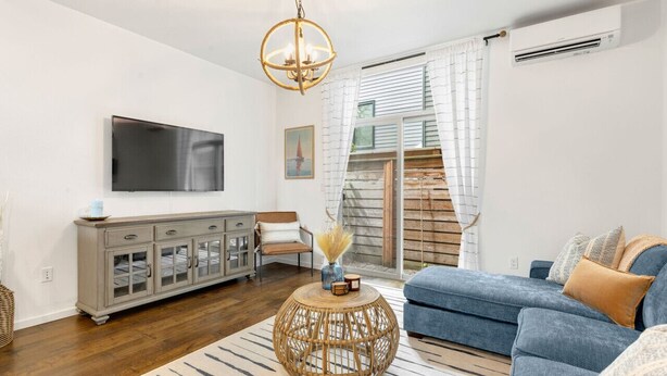 A modern living room with a blue sofa, a round wicker coffee table, a grey cabinet, and a flat-screen TV mounted on the wall.