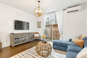 A modern living room with a blue sofa, a round wicker coffee table, a grey cabinet, and a flat-screen TV mounted on the wall.