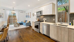 A modern kitchen with stainless steel appliances, a large window with a view of trees, and a dining area with a blue sofa and wooden table.