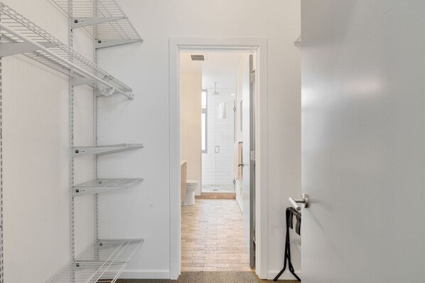 A narrow hallway with metal shelving units on the left, leading to a bathroom with a toilet and shower area.