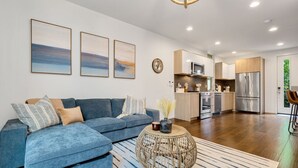 A modern living room with a sectional sofa, a round coffee table, and a kitchen in the background.