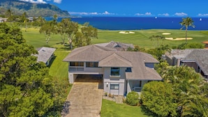 Une maison à deux étages avec un grand jardin à l’avant et une vue sur un terrain de golf et l’océan.