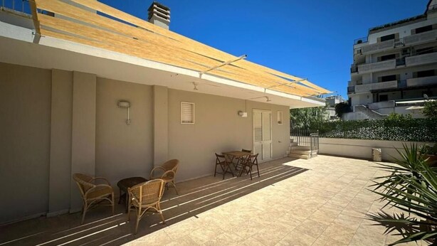 A covered outdoor area with a table and chairs, a tiled floor, and a building with a flat roof in the background. - Andromeda Rooms  in Otranto (Otranto)
