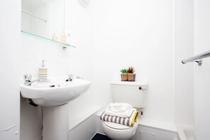 A small, white bathroom with a white sink, a toilet, and a glass shelf above the sink. - Student Only Exchange Works (Sheffield)