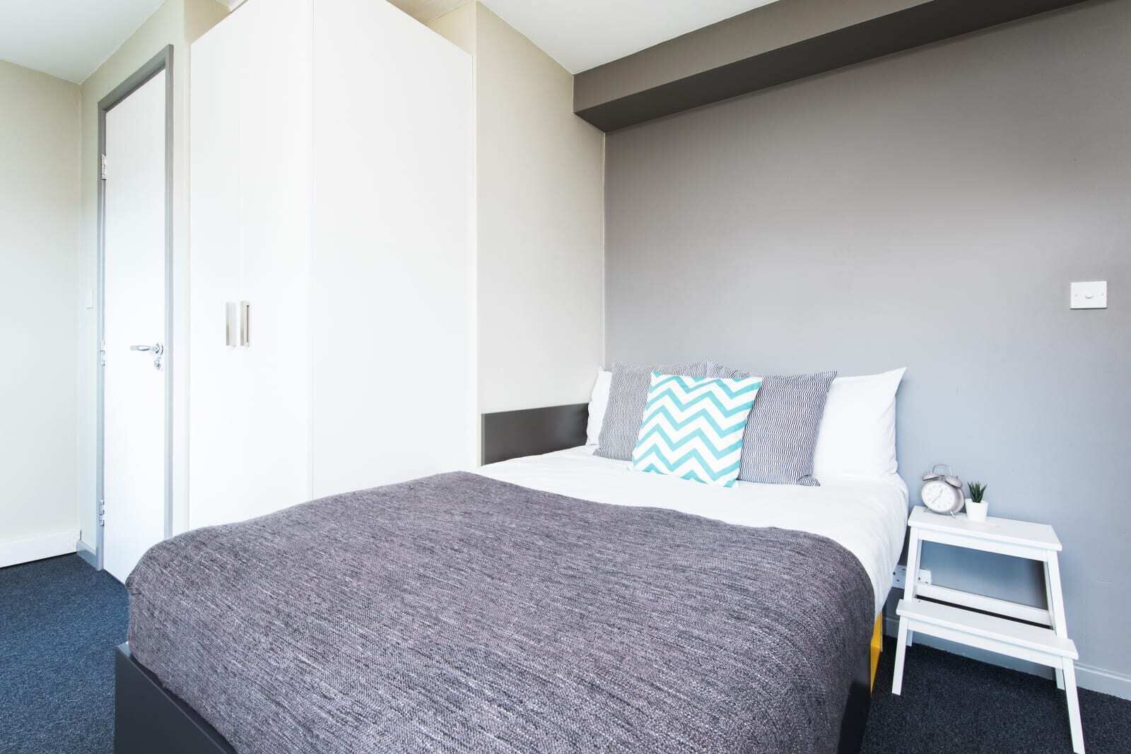 Una habitación de hotel con una cama, una mesita de noche, un reloj y una puerta.