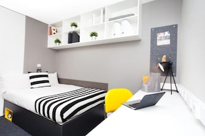 A modern bedroom with a bed, a desk with a laptop, a yellow chair, a bookshelf, and a wall-mounted lamp. - Student Only Exchange Works (Sheffield)