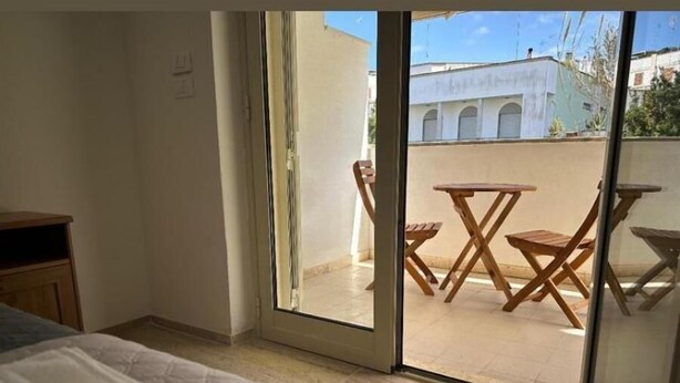 Un dormitorio con una cama, una mesita de noche de madera y una puerta corrediza de vidrio que da a un patio exterior con una mesa y sillas.