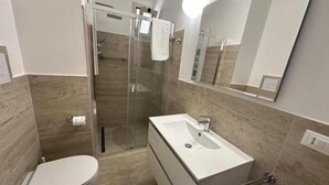 Un baño moderno con ducha acristalada, lavabo blanco y retrete.
