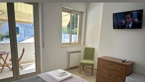 Un dormitorio con una cama, una silla verde, un aparador de madera, un televisor y una ventana con vistas al exterior.