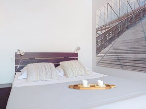 A bedroom with a bed, pillows, a tray with cups and cookies, and a wall-mounted picture of a bridge. - Le Mascoïnat by Interhome (Nice)