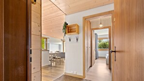 Um interior moderno com piso de madeira, uma área de jantar com mesa e cadeiras, e vista para o exterior através de uma grande janela.