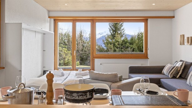 Uma sala de estar moderna com sofá, mesa de jantar e janelas amplas com vista para as montanhas.