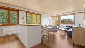 Uma cozinha moderna com armários de madeira, uma sala de jantar com mesa e cadeiras, e um espaço de estar aconchegante com um sofá e uma mesinha.