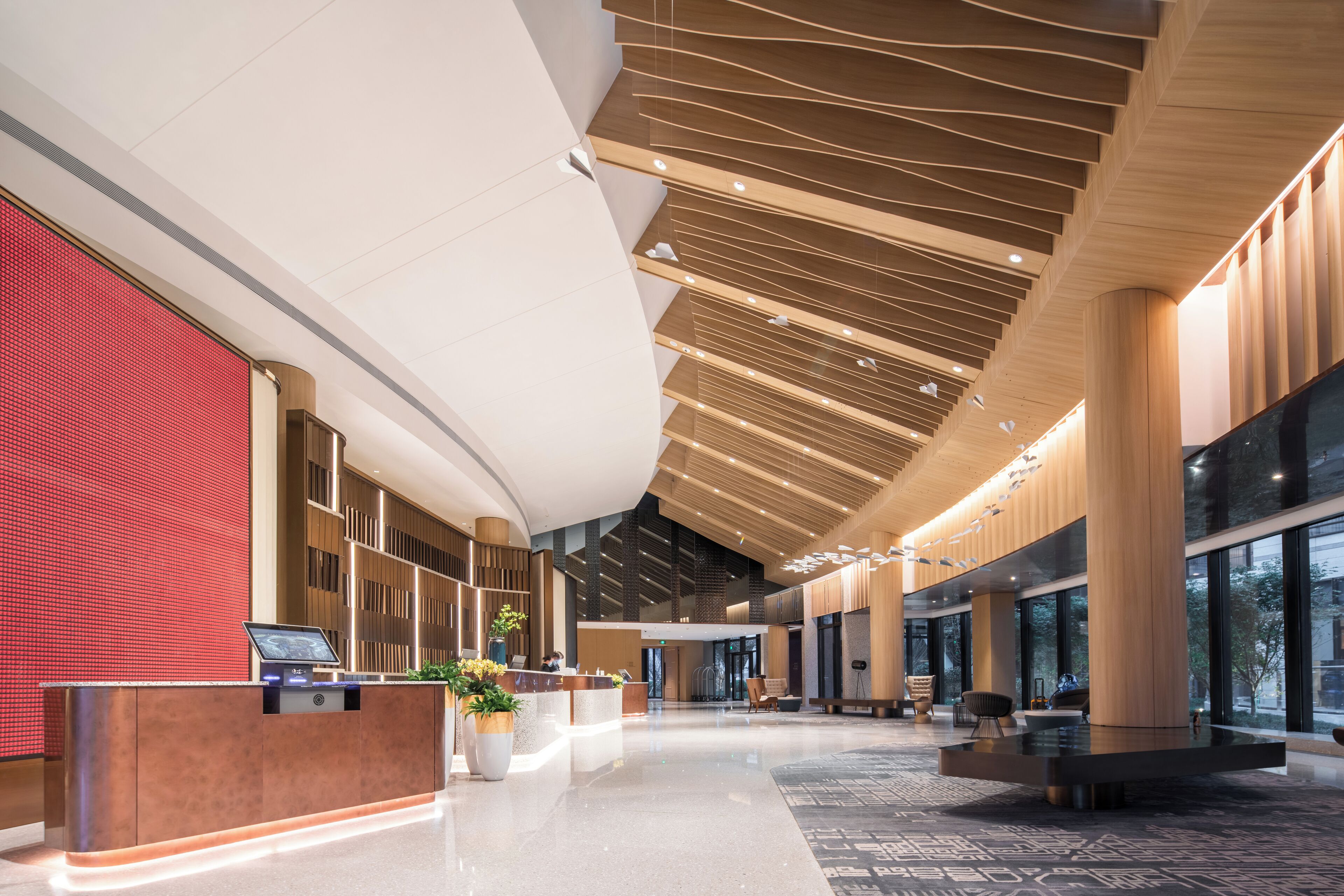 A spacious lobby with a modern design, featuring a reception desk, seating areas, and large windows.