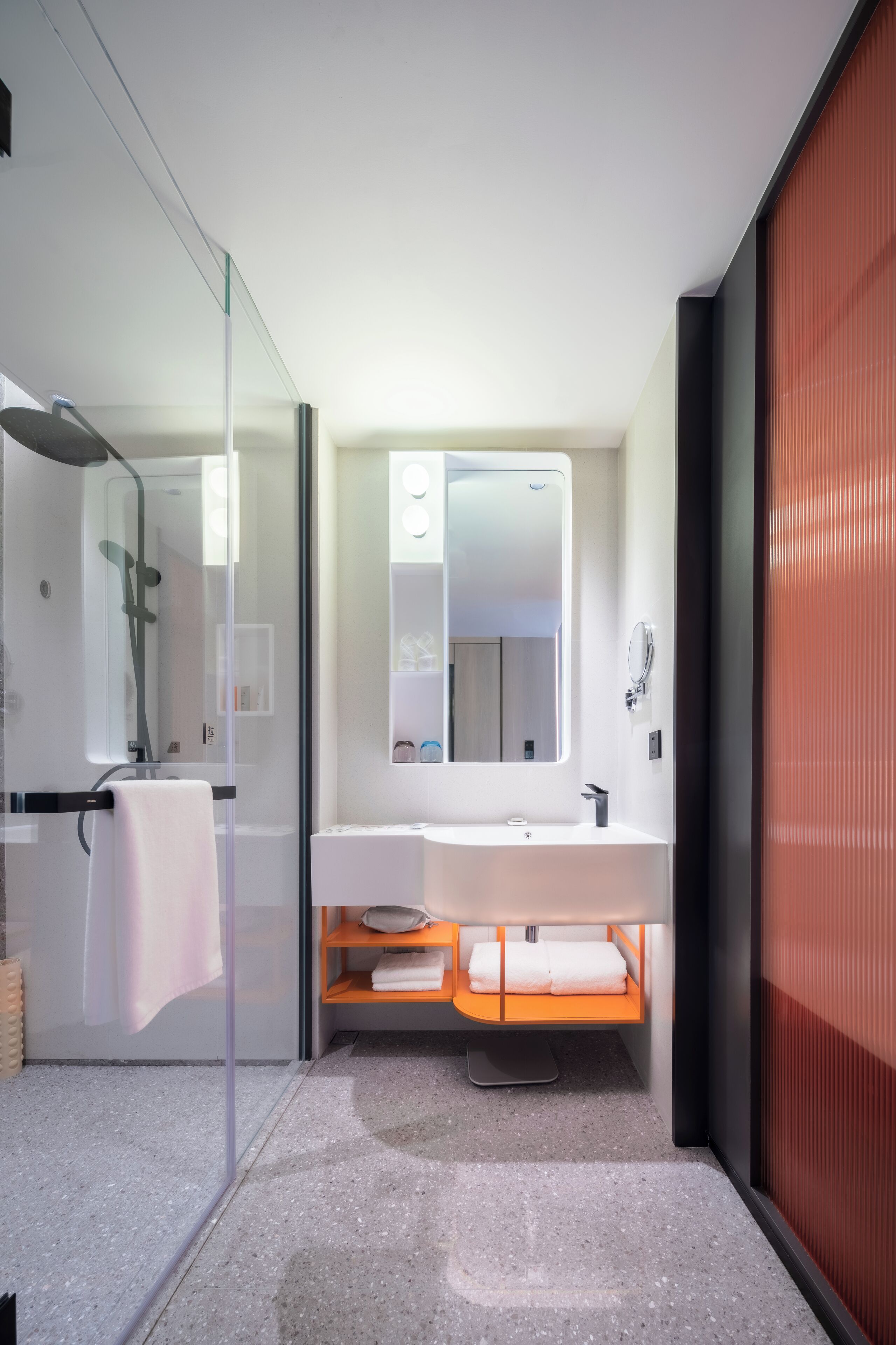 Ein modernes Badezimmer mit Duschkabine aus Glas, einem weißen Waschbecken mit Spiegel darüber und einer roten Akzentwand.
