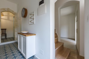 A hallway with a white cabinet, a bowl on top, a patterned floor, a wooden staircase, and an arched doorway.