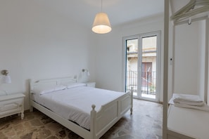 A bedroom with a bed, bedside tables, a hanging light fixture, a balcony door, and a view of the outside.