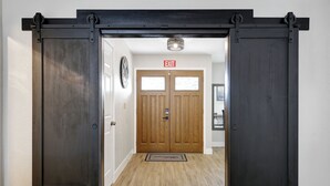 A hallway with a wooden door marked "EXIT" and a doormat. - Ultimate Retreat | Game Room Fire Pit BBQ Office (San Antonio)