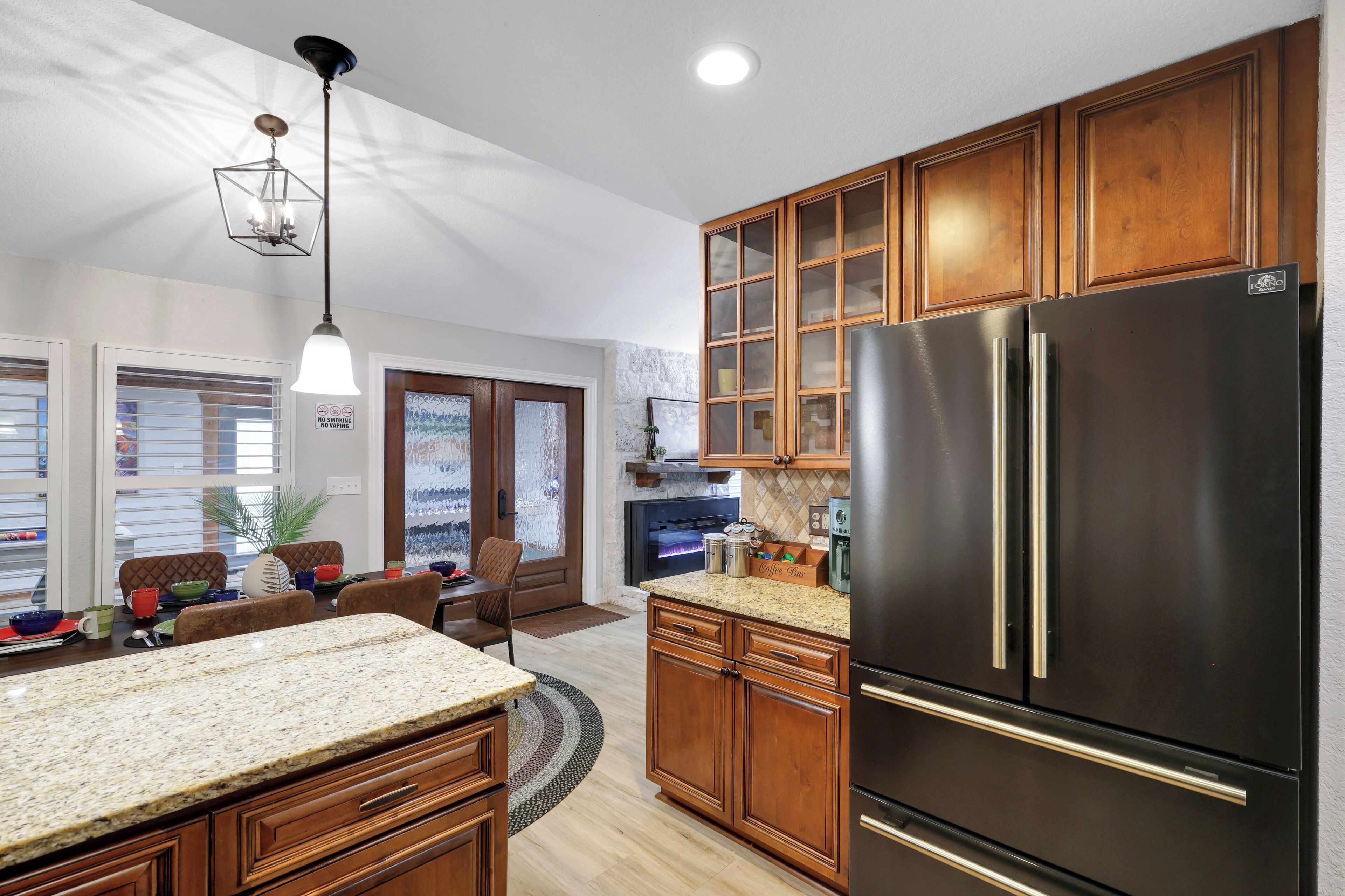 A kitchen with wooden cabinets, a black refrigerator, and a granite countertop. - Ultimate Retreat | Game Room Fire Pit BBQ Office (San Antonio)