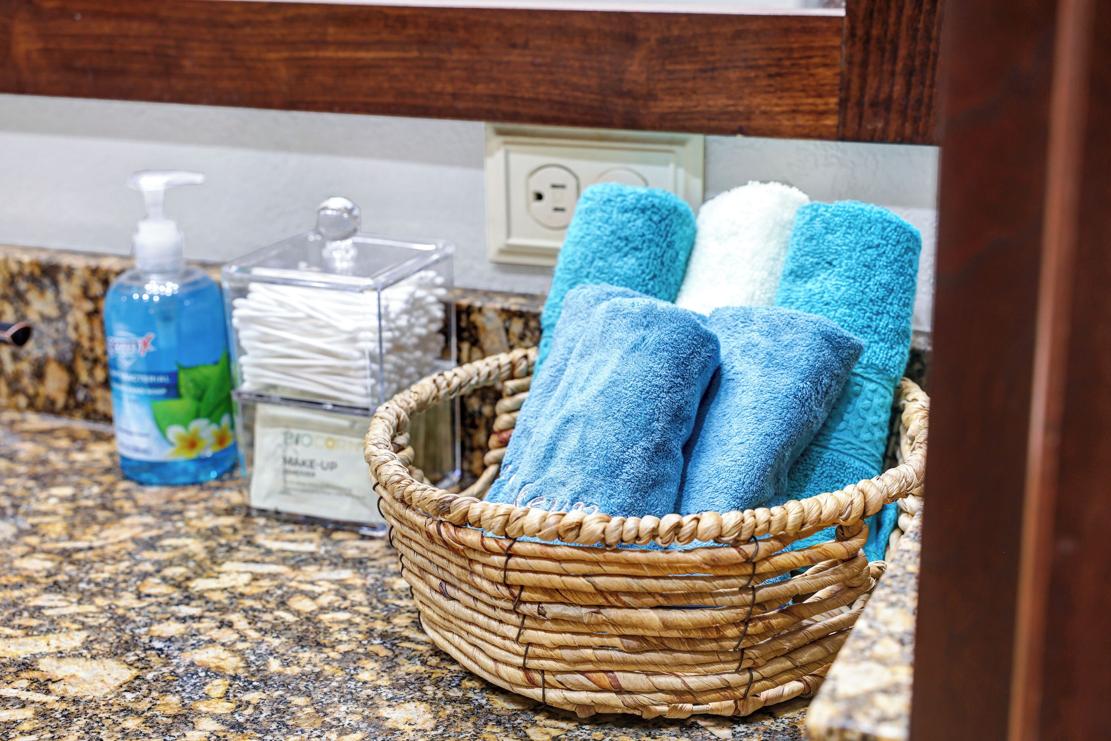 A bathroom with a woven basket containing towels, a soap dispenser, and a container of cotton swabs.